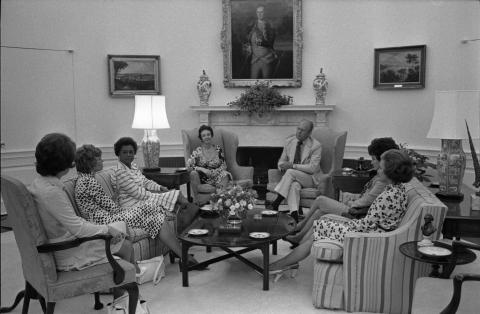 A group of people sitting on couches in a semi-circle in the White House Oval Office.