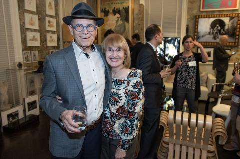 A man and woman standing closely together in a room filled with people socializing.