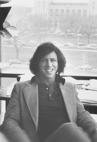 A young man with long hair smiles at the camera.