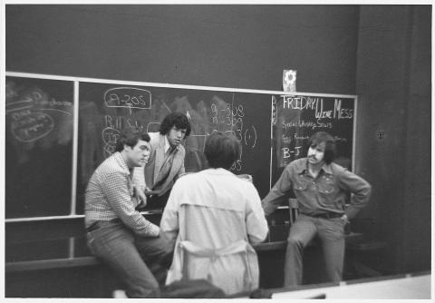 Men standing in front of chalkboard in deep conversation.