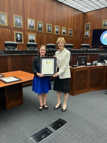 Two women standing side by side, one is holding an award
