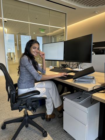 Amrita sits at a desk in professional attire.