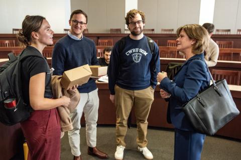 Four people standing in a classroom, looking at each other and talking.
