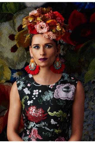 Regina Myerson wears a floral dress with flowers in her hair and statement earrings.