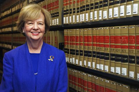 Judith Wright, wearing a blue blouse and suit, smiles, with casebooks behind her.