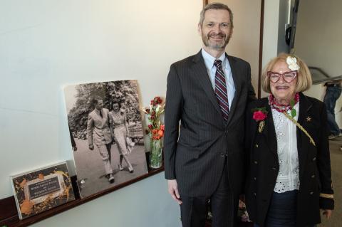 Hombre y mujer sonriendo a la cámara con tablero blanco, flores y tableros de carteles de fotos.