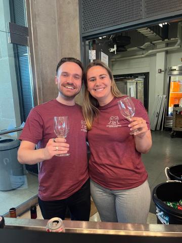 Liam Haffey and a fellow student, wearing matching shirts, raise empty wine glasses.