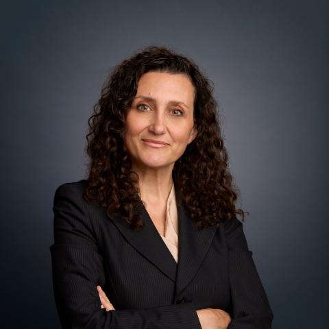 Professional headshot of Sandra Frantzen wearing a dark suit and beige blouse. Her hands are folded across her body.