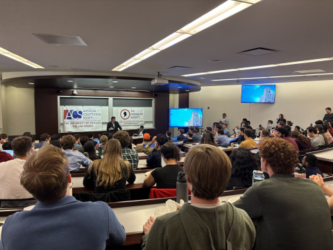 Far view of Will Baude presenting, with large crowd of students looking on