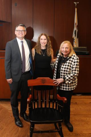 Alison Siegler poses with Dean Adam Chilton and Lillian Kraemer in front of a wooden chair.