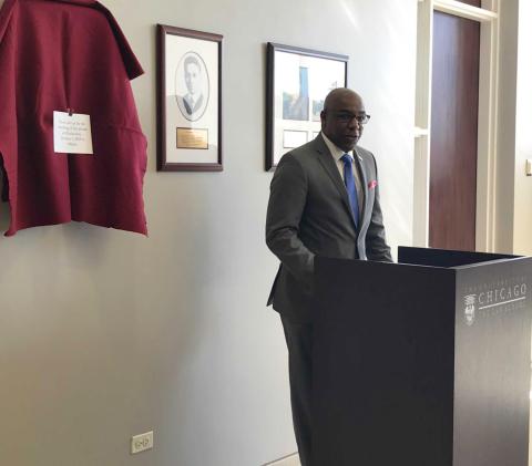 A middle aged Black man stands in front of a podium inside the Law School hallway.