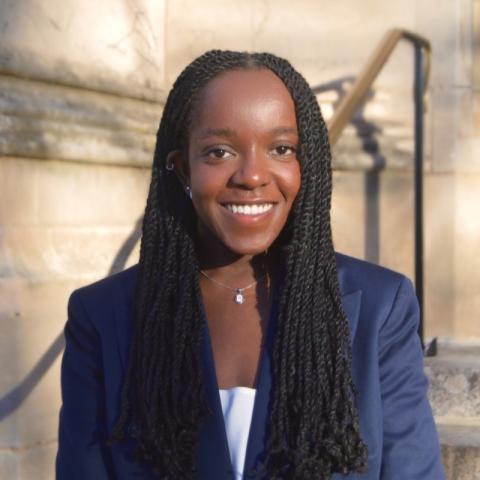 A young Black woman smiles warmly in a navy blue blazer.
