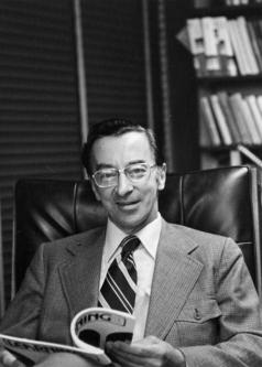 Black and white photograph of Norval Morris flipping through a magazine at his desk.