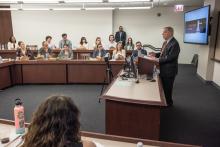 Senator Durbin stands in the front of a classroom behind a podium. Student are seated in background.