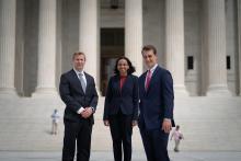 Three people in professional attire stand in front of the Supreme Court building