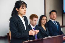 A person standing at a podium with 3 people sitting close to her