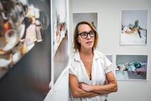 Professor Laura Letinsky leaning against a wall near a corner of the room with a lot of paintings around