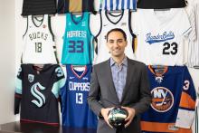 Daniel Render holds a ball with jerseys from the Hornets, ThunderBolts, Clippers, and NY Islanders, and Bucks behind him.