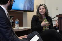 A woman gesturing while she speaks to a man seated next to her in a classroom.
