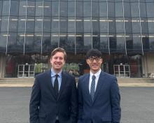 Two men wearing suits standing in front of a large glass building.