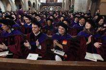 Seated in pews, graduates in caps and gowns applaud their classmates.