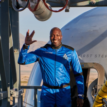 In a blue jumpsuit in front of the entrance bridge to a rocket cockpit, Jaison Robinson makes a Star Trek sign.