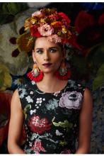 Regina Myerson wears a floral dress with flowers in her hair and statement earrings.