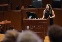 Alison Siegler stands at the lecturn addressing the audience. A partial view of the audience is in the photo.