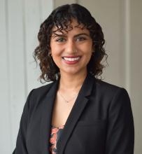 A professional headshot of Vatsala Kumar, a woman with dark, short curly hair. She is wearing a black blazer.