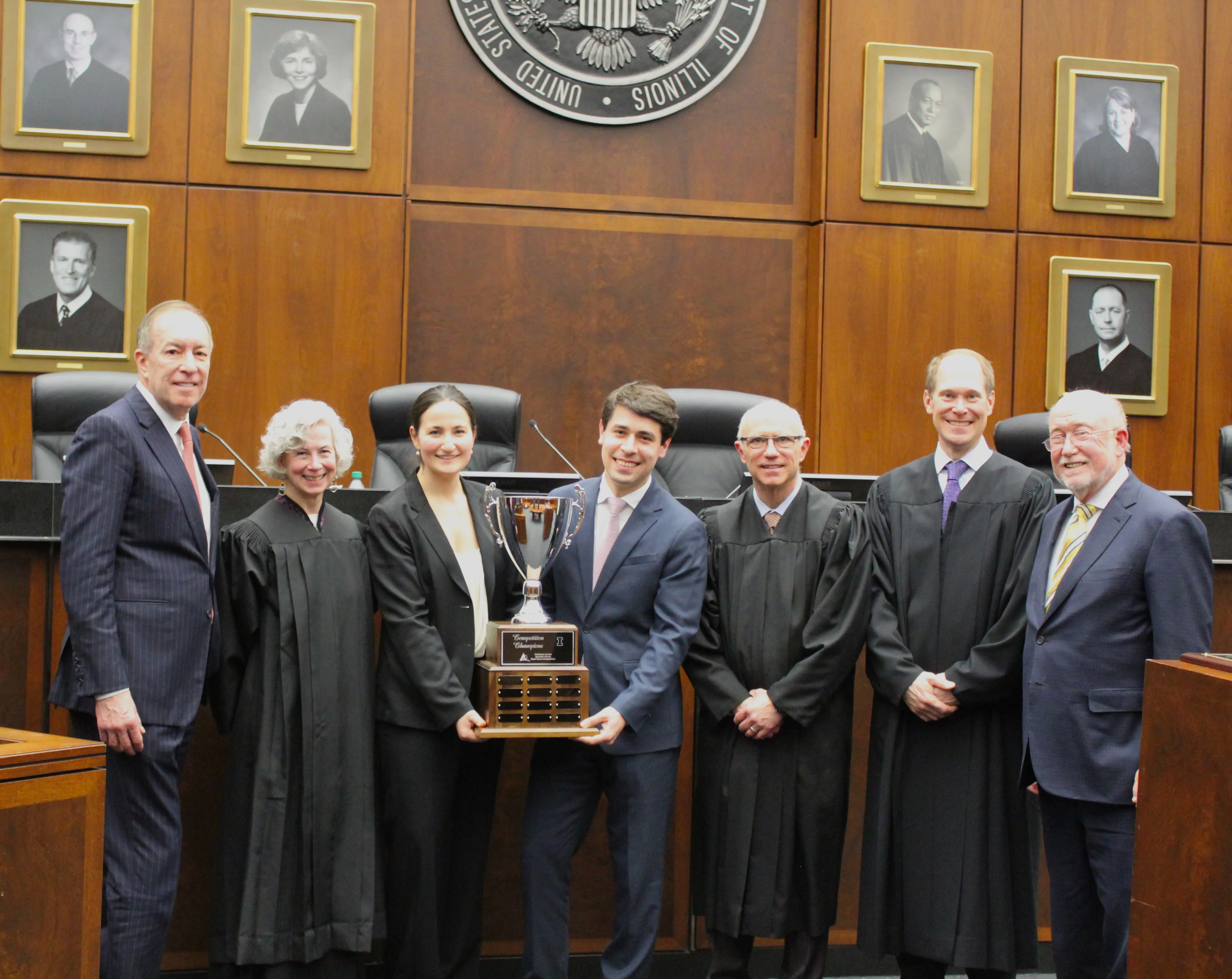 Students hold their trophy flanked by judges and co-chairs of the competition