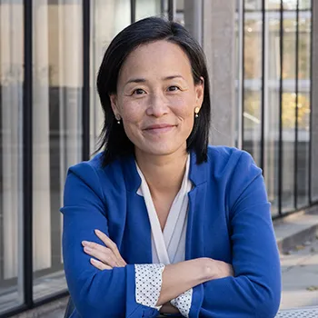 Jennifer Nou sits a table outside, arms crossed. She wears a white blouse and blue blazer.