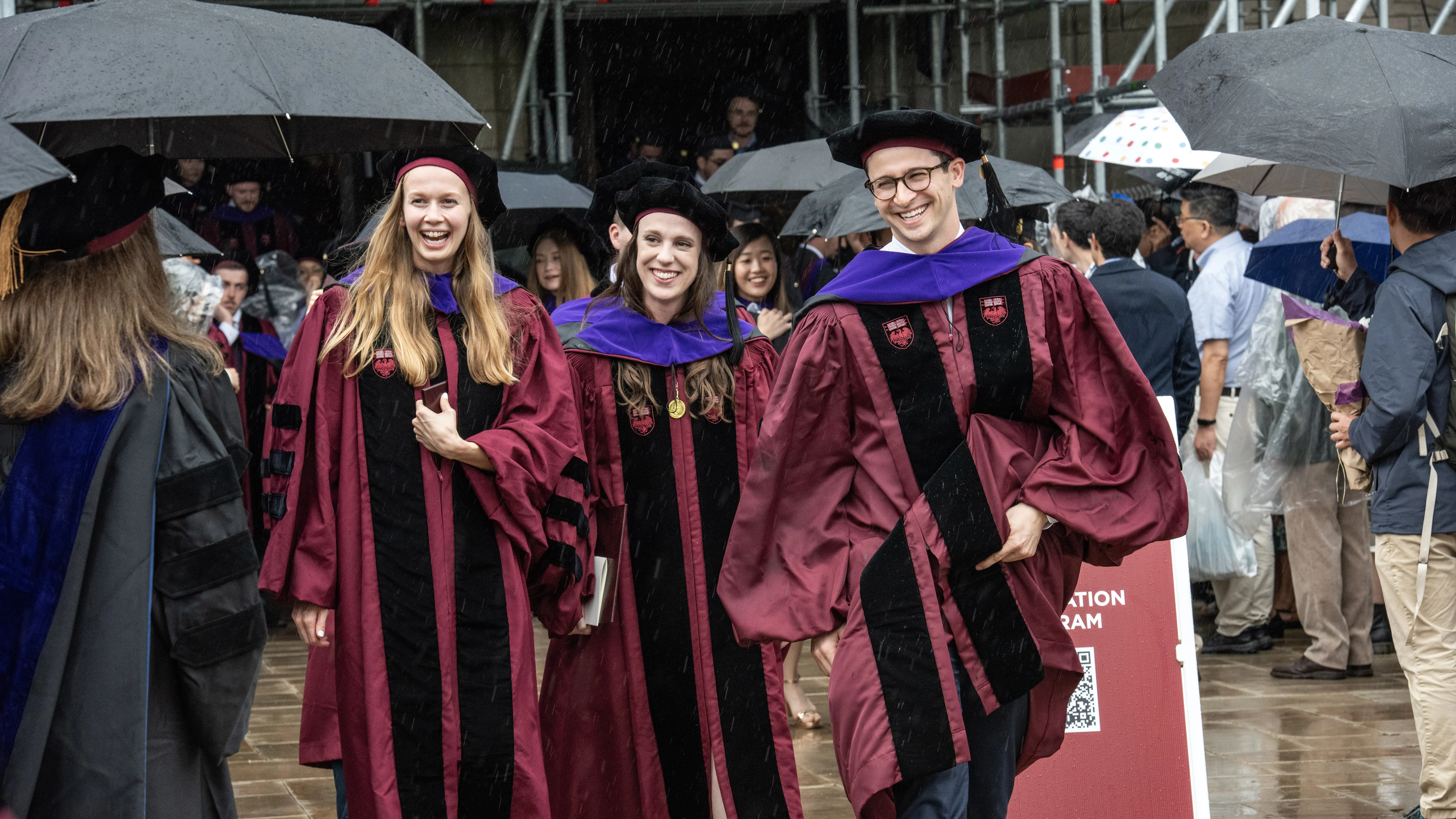 Students smiling in their caps and gowns exit Rockefeller Memorial Chapel admist the rain.