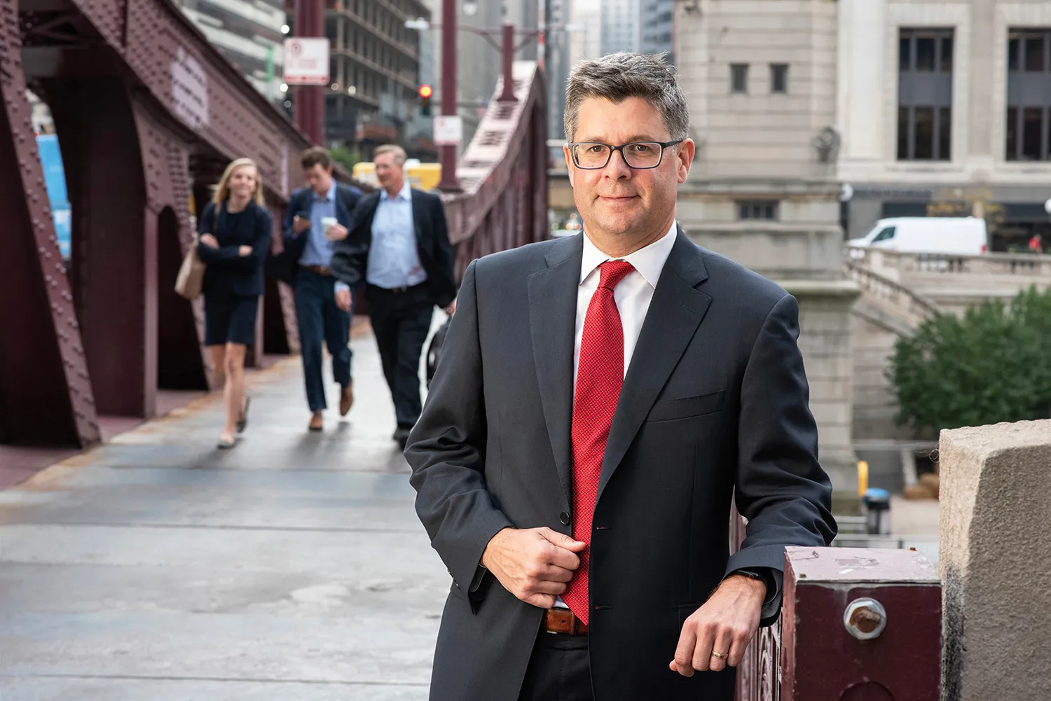 Brent Rogers, in a dark suit and red tie, stands in an urban setting.