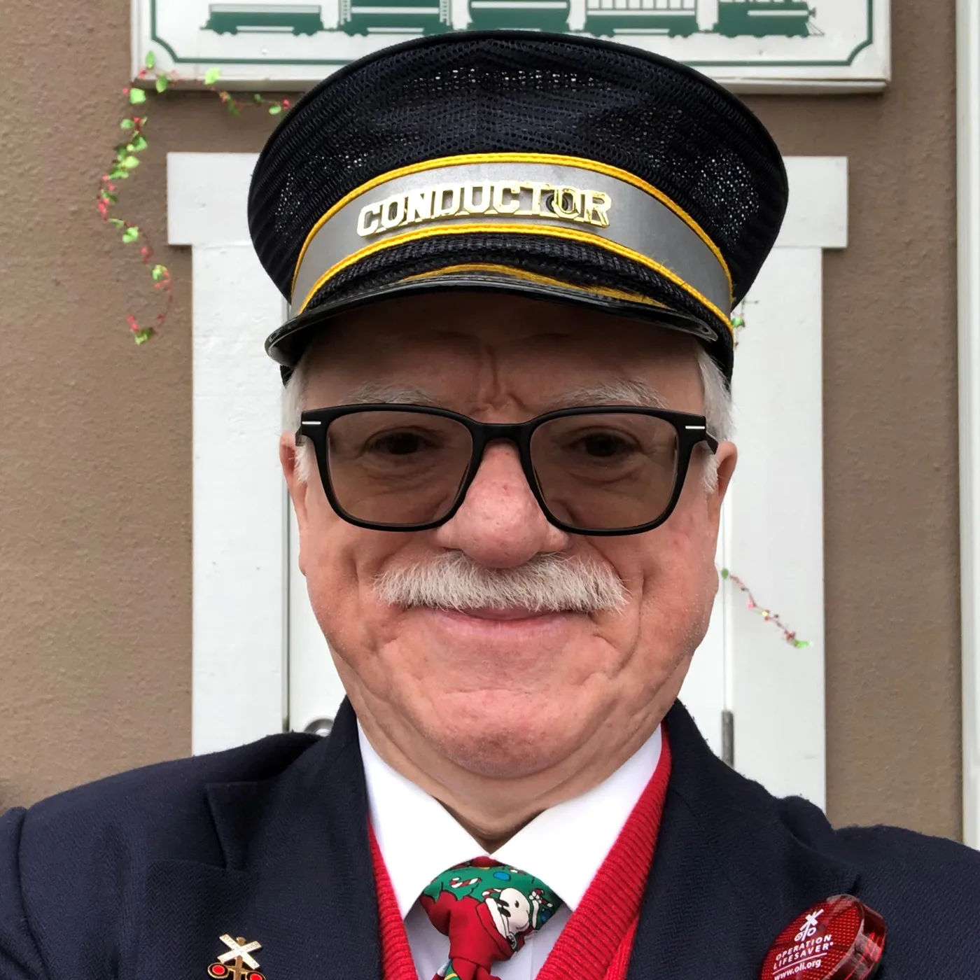 David Applegate takes a self in a suit, tie, and sweater vest with a conductor's hat on.