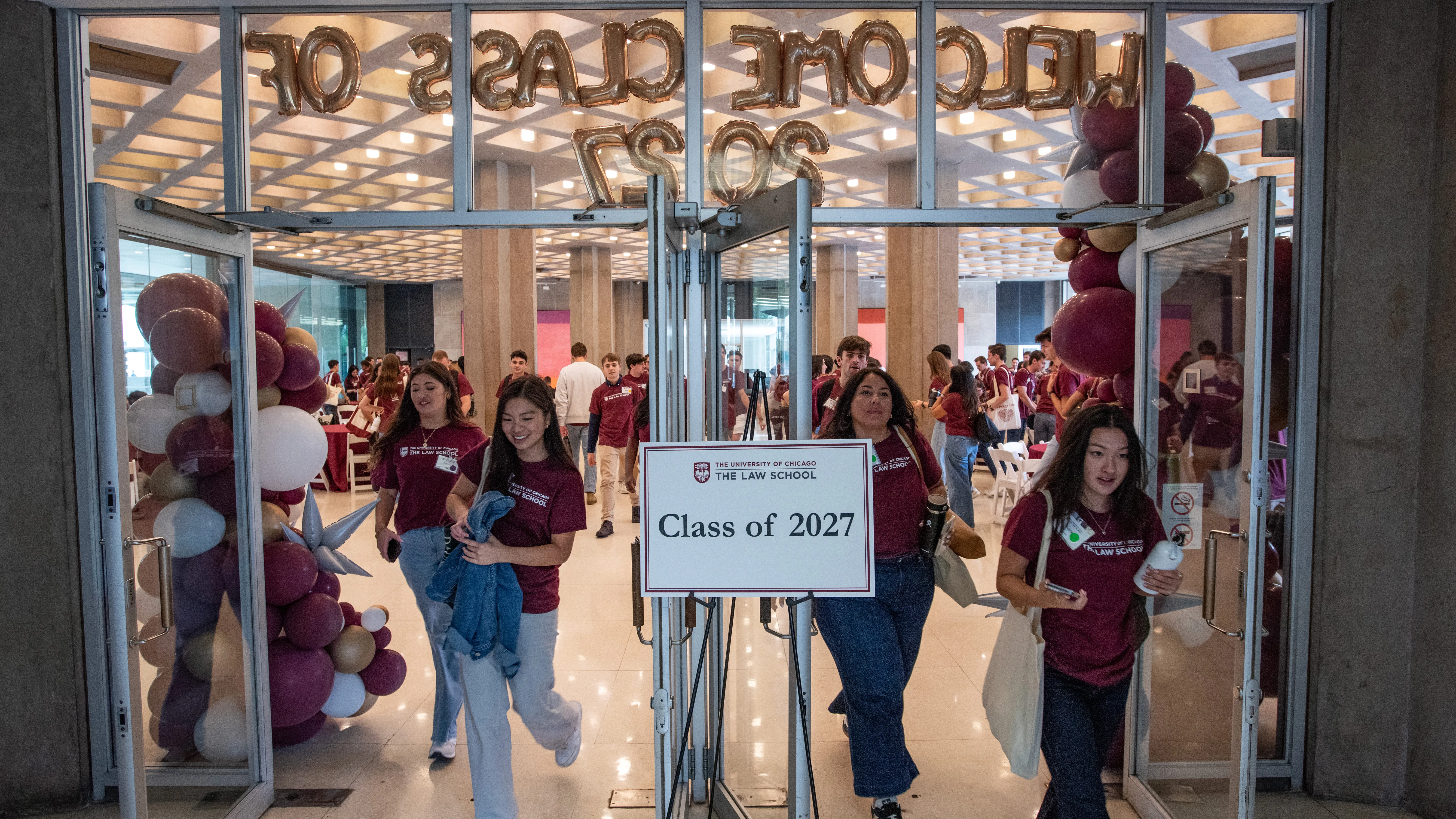 New 1Ls in matching maroon shirts at orientation stream through the Green Lounge. A sign says Class of 2027.