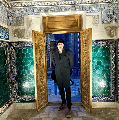 Kirby Voss stands in an ornate doorway in a black overcoat and hat.