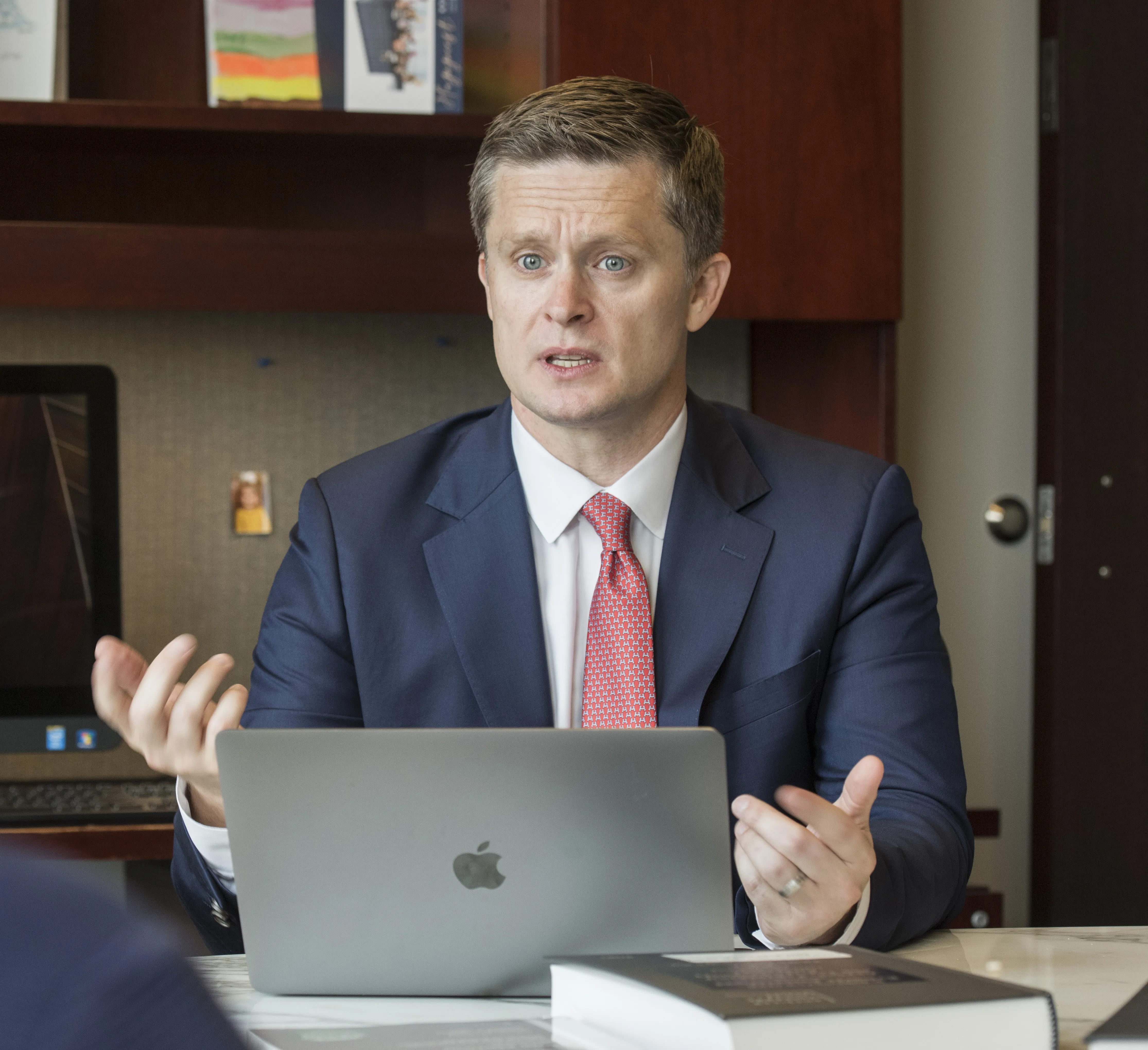 Casey wearing a suit in front of a laptop talking