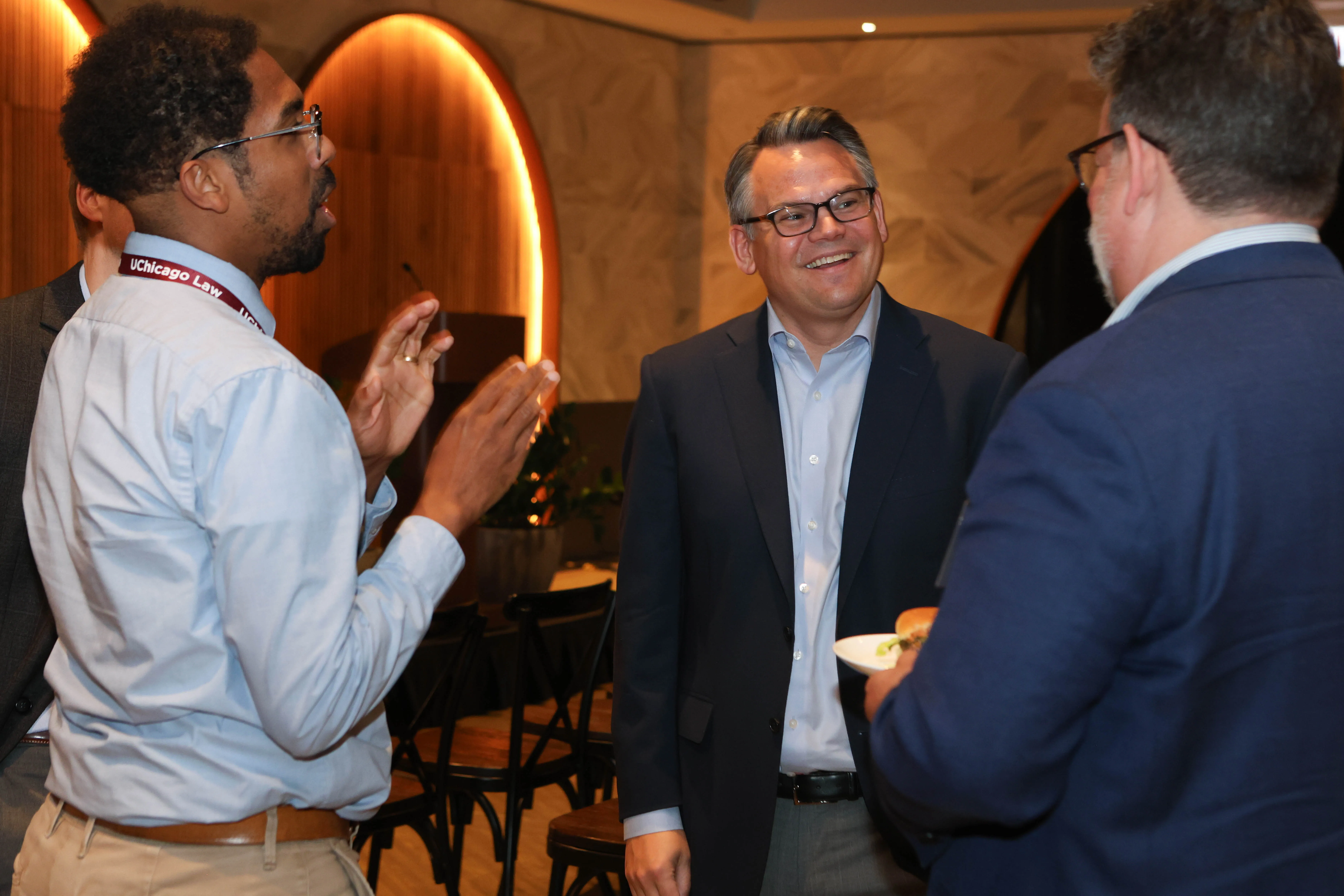 The dean stands in front of two male alumni chatting and smiling with them