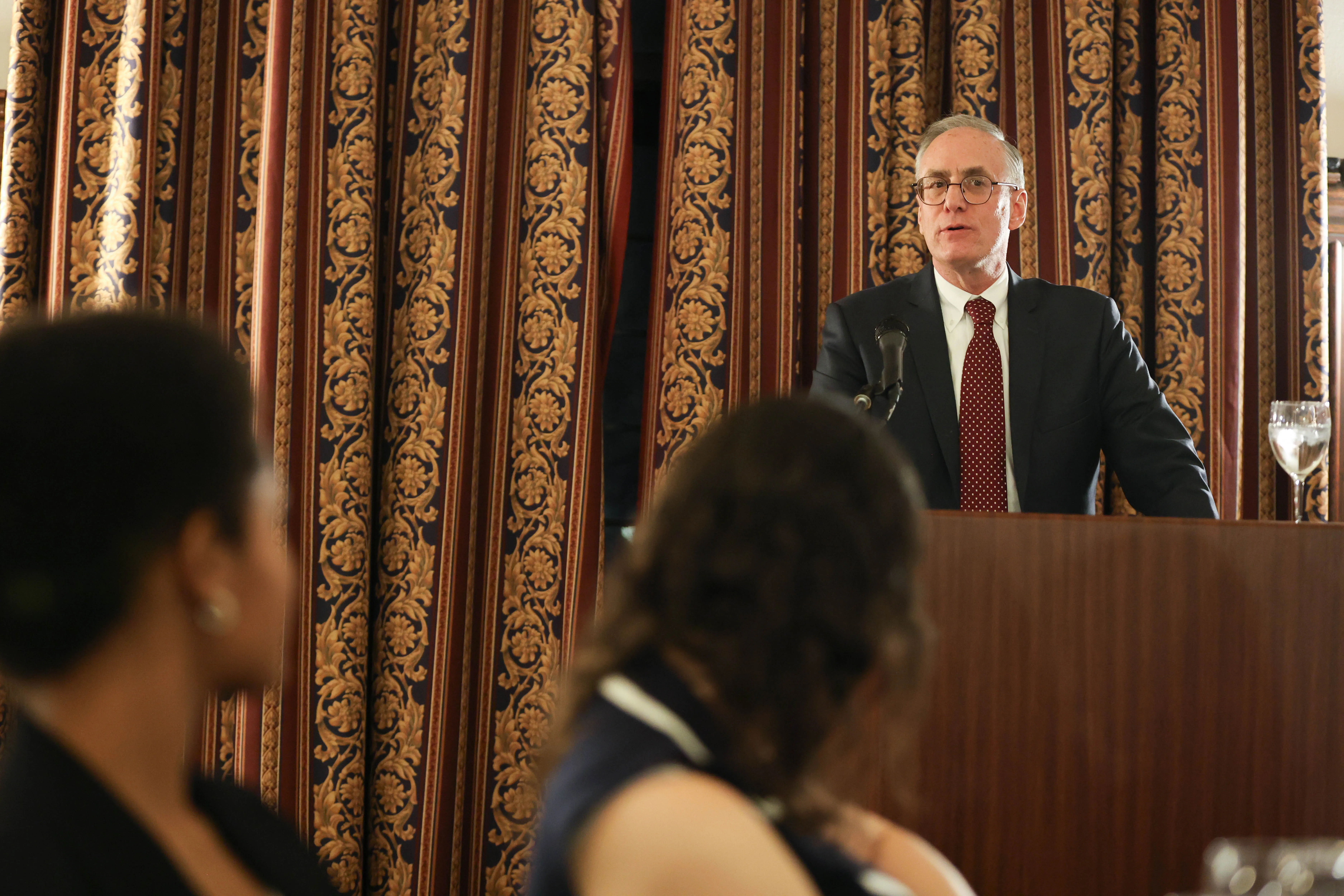 Professor Curtis Bradley, dressed in a dark grey suit and maroon tie, speaks to a crowded room.